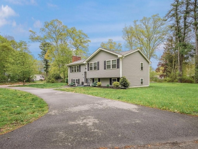 raised ranch featuring a chimney, a front lawn, and asphalt driveway