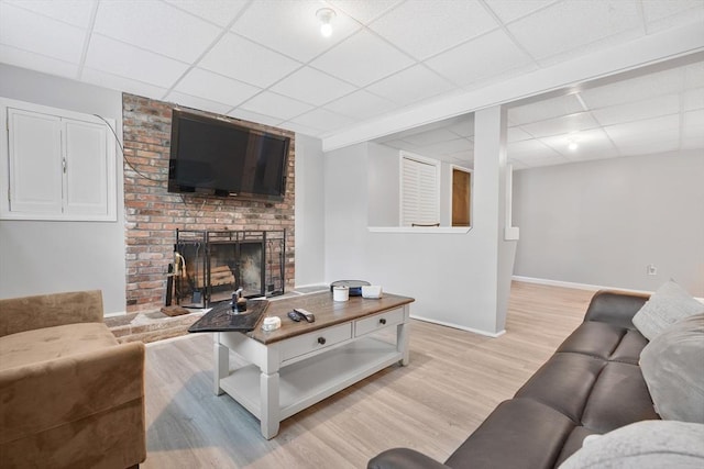 living area with a paneled ceiling, light wood-style floors, baseboards, and a brick fireplace