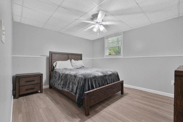 bedroom featuring wood finished floors, a drop ceiling, a ceiling fan, and baseboards