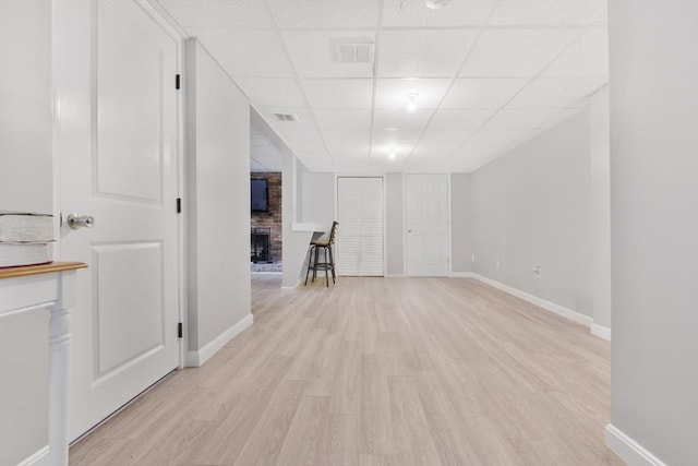 unfurnished living room featuring a fireplace, a paneled ceiling, baseboards, and light wood finished floors