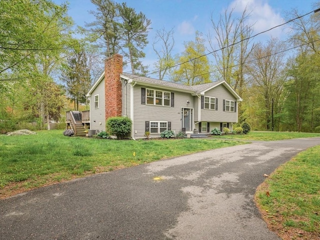 raised ranch with a chimney, a front yard, asphalt driveway, and a deck