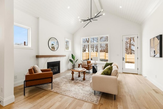 living room with baseboards, an inviting chandelier, light wood-style floors, high vaulted ceiling, and a high end fireplace