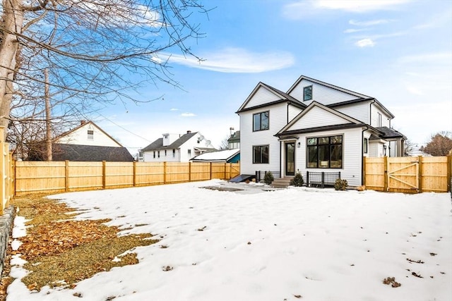 snow covered rear of property with a fenced backyard and a gate