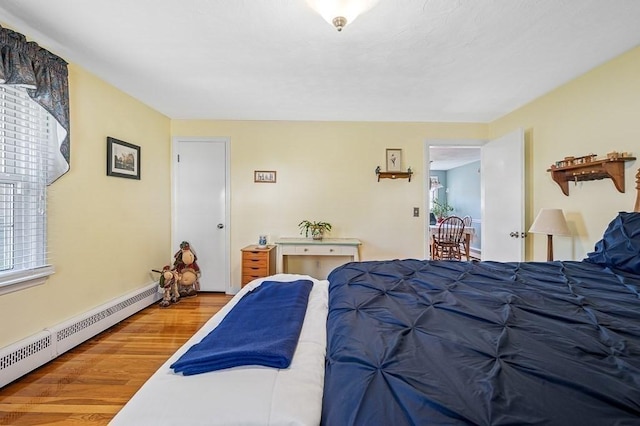 bedroom with baseboards, a baseboard radiator, wood finished floors, and multiple windows