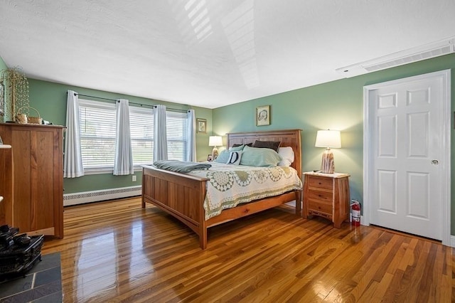 bedroom with a baseboard heating unit, wood finished floors, and visible vents