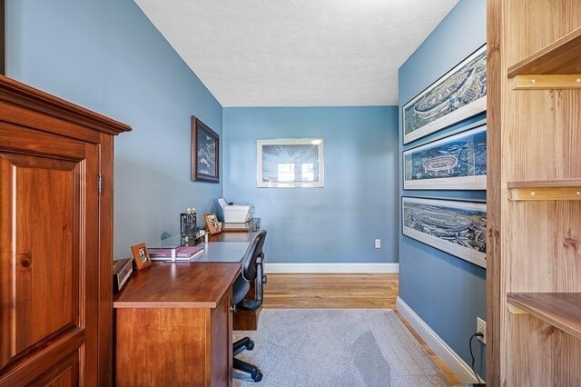 office area with a textured ceiling, baseboards, and light wood finished floors