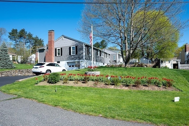view of property exterior featuring a garage, aphalt driveway, a yard, and a chimney