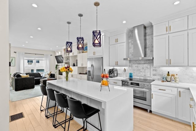 kitchen with wall chimney range hood, stainless steel appliances, light wood finished floors, and visible vents