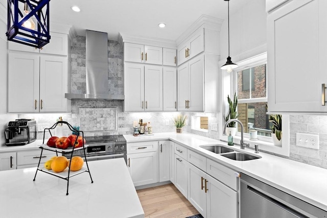 kitchen with wall chimney range hood, light countertops, white cabinetry, a sink, and stainless steel appliances