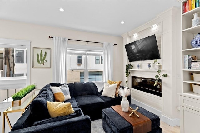 living room featuring a glass covered fireplace, built in features, recessed lighting, and light wood-style flooring