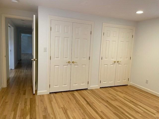 unfurnished bedroom with multiple closets, light wood finished floors, baseboards, and recessed lighting