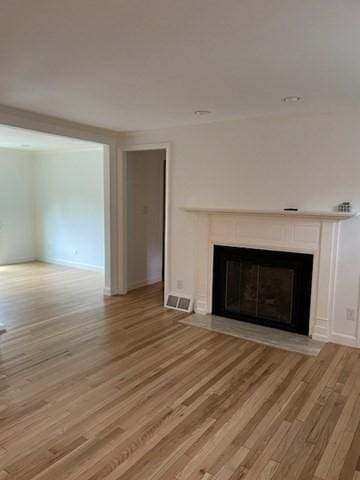 unfurnished living room with a fireplace with flush hearth, light wood-type flooring, and baseboards