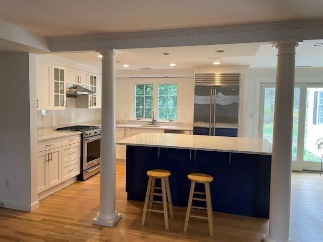 kitchen with decorative columns, appliances with stainless steel finishes, a sink, backsplash, and light wood-style flooring