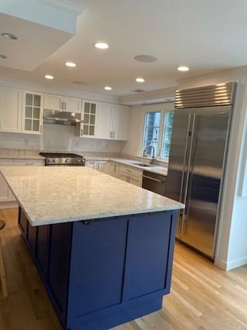 kitchen with built in fridge, under cabinet range hood, a center island, light wood finished floors, and glass insert cabinets