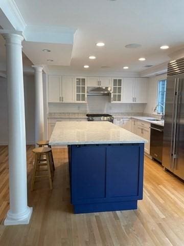 kitchen featuring high end fridge, ornate columns, dishwashing machine, white cabinetry, and under cabinet range hood