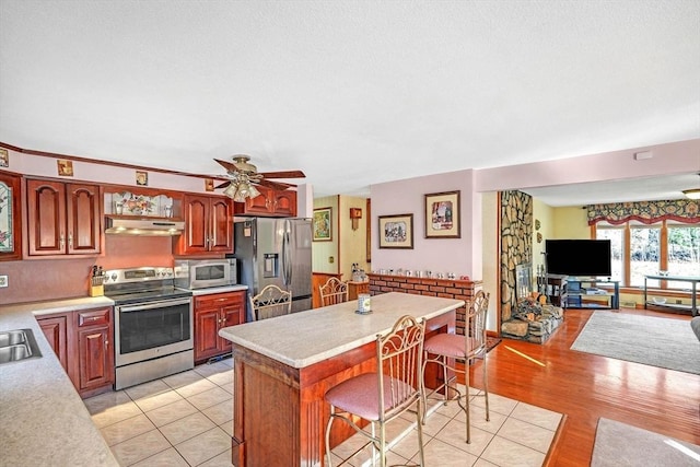 kitchen with appliances with stainless steel finishes, ceiling fan, light tile patterned floors, a kitchen island, and a breakfast bar area