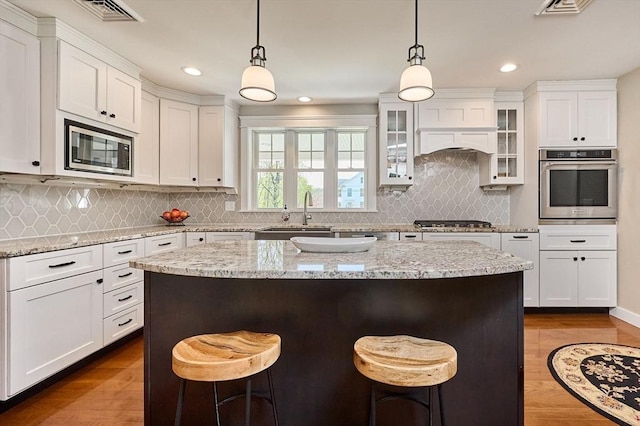 kitchen featuring appliances with stainless steel finishes, a sink, a kitchen breakfast bar, dark wood finished floors, and white cabinetry