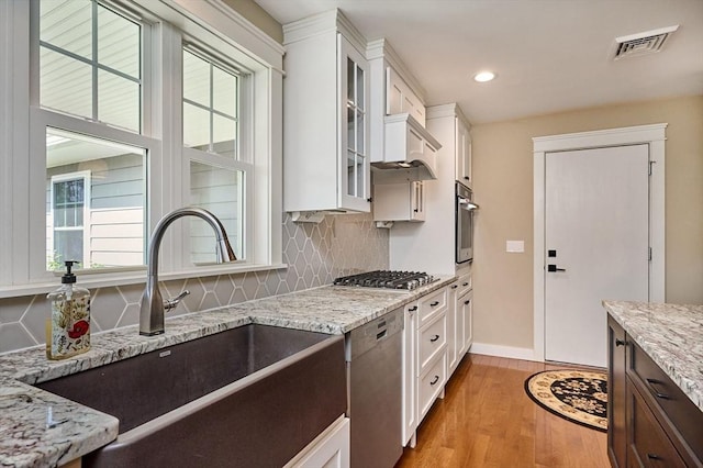 kitchen with a sink, light wood-style flooring, stainless steel appliances, white cabinetry, and visible vents