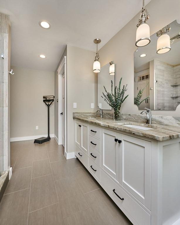 full bath with a sink, baseboards, a stall shower, and double vanity