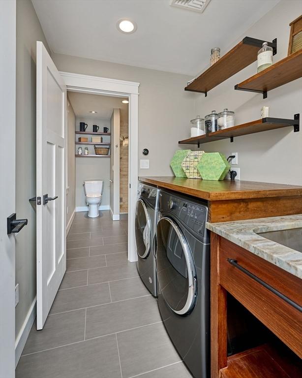 washroom with washing machine and clothes dryer, dark tile patterned flooring, baseboards, and laundry area