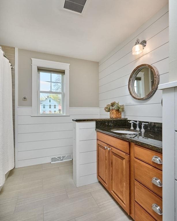 bathroom featuring vanity, wainscoting, wood walls, and visible vents
