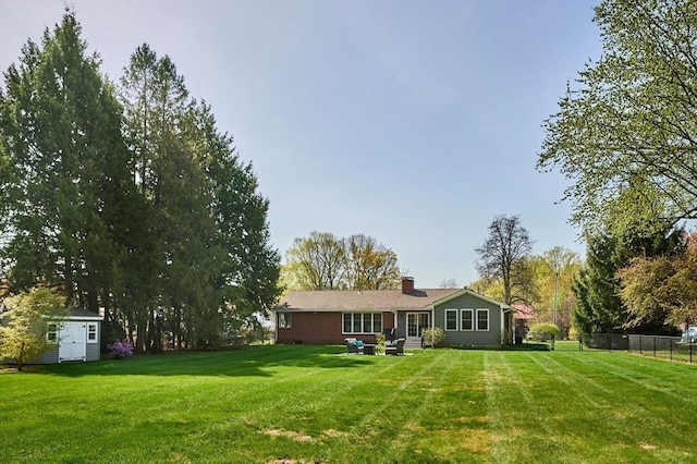 back of house with fence, a storage shed, an outbuilding, a chimney, and a lawn