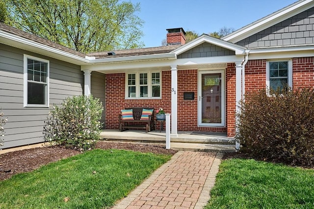 view of exterior entry with a chimney, a porch, and brick siding