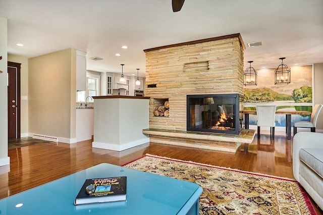 living room with a stone fireplace, visible vents, baseboards, recessed lighting, and hardwood / wood-style floors