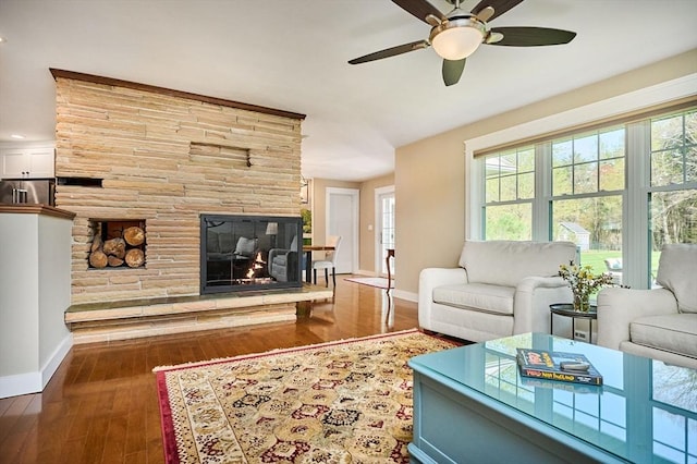living room with baseboards, a stone fireplace, ceiling fan, and hardwood / wood-style floors