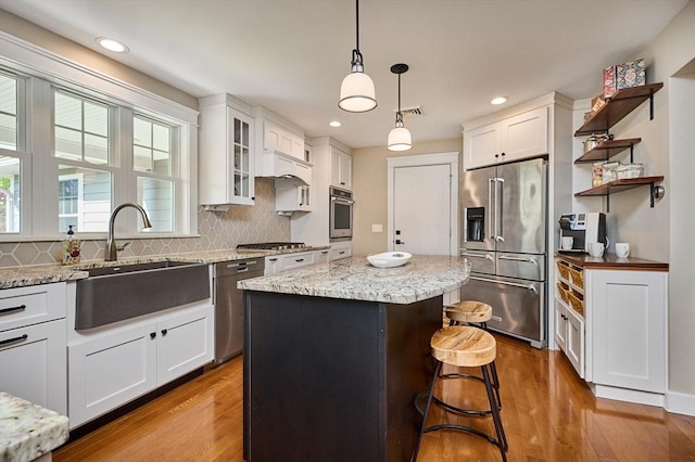 kitchen with a sink, stainless steel appliances, decorative backsplash, wood finished floors, and a kitchen island