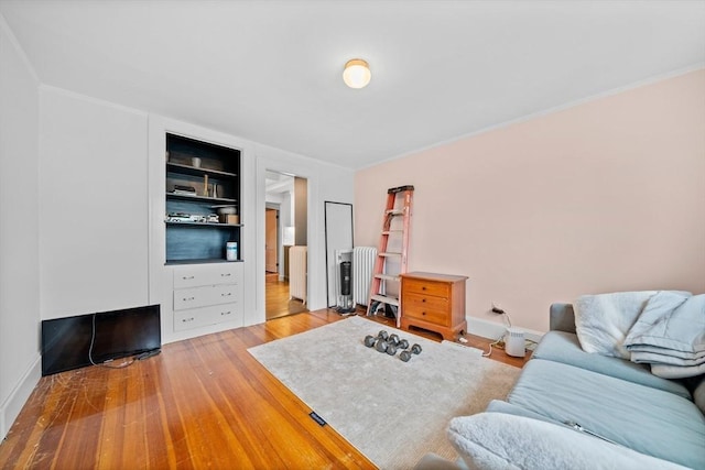 living area with built in features, crown molding, wood finished floors, radiator heating unit, and baseboards