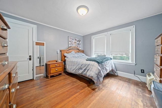 bedroom with radiator, light wood-style floors, crown molding, and baseboards