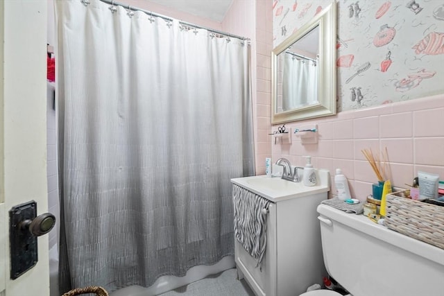 bathroom with wallpapered walls, toilet, tile walls, vanity, and a wainscoted wall