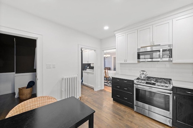 kitchen featuring stainless steel appliances, radiator, dark cabinets, white cabinetry, and a wainscoted wall