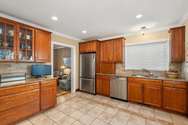 kitchen with glass insert cabinets, ornamental molding, appliances with stainless steel finishes, brown cabinetry, and a sink