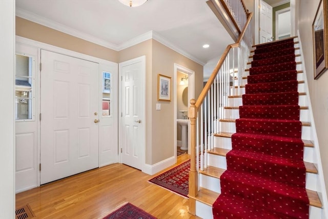 entrance foyer with visible vents, ornamental molding, wood finished floors, baseboards, and stairs