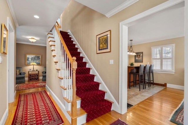 stairway with wood finished floors, baseboards, and ornamental molding