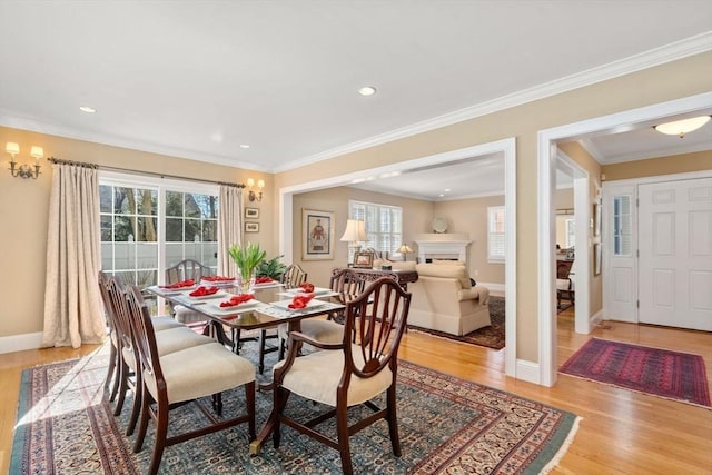 dining room with light wood finished floors, crown molding, baseboards, recessed lighting, and a fireplace