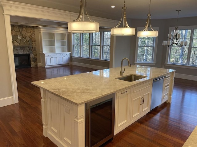 kitchen with light stone countertops, decorative light fixtures, beverage cooler, and an island with sink