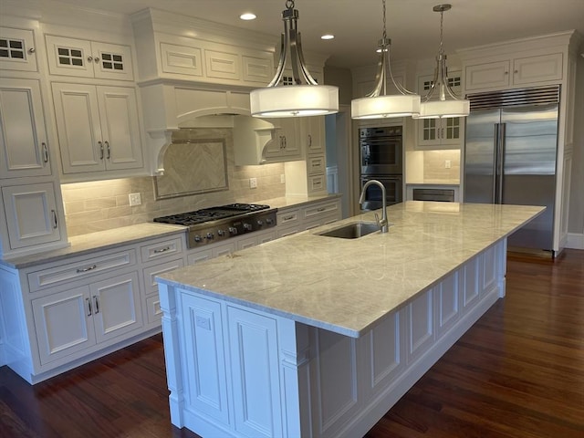 kitchen with white cabinetry, sink, stainless steel appliances, decorative light fixtures, and a center island with sink