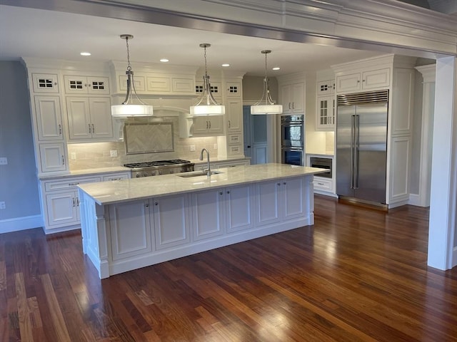 kitchen with sink, built in appliances, white cabinetry, hanging light fixtures, and an island with sink