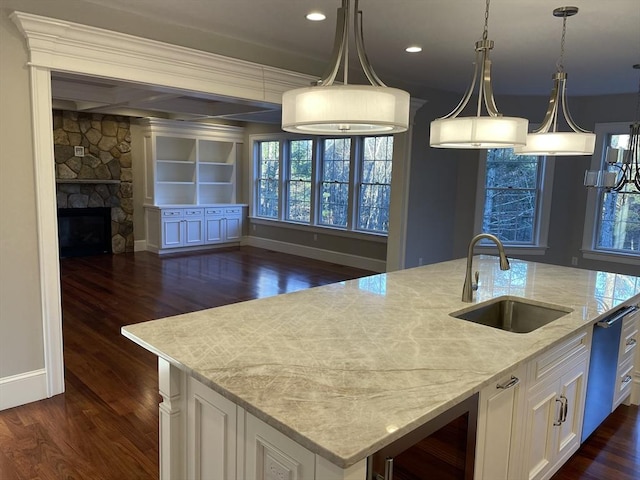 kitchen with a fireplace, light stone countertops, sink, and a kitchen island with sink