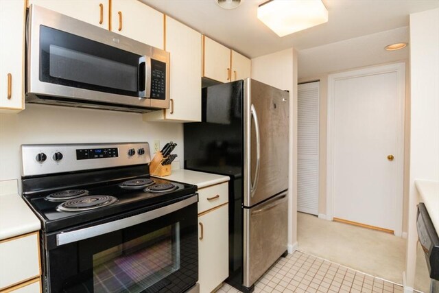 kitchen with light colored carpet, appliances with stainless steel finishes, light countertops, baseboards, and light tile patterned floors