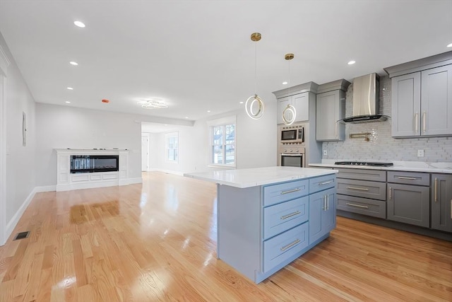 kitchen with stainless steel appliances, wall chimney range hood, tasteful backsplash, light hardwood / wood-style flooring, and decorative light fixtures