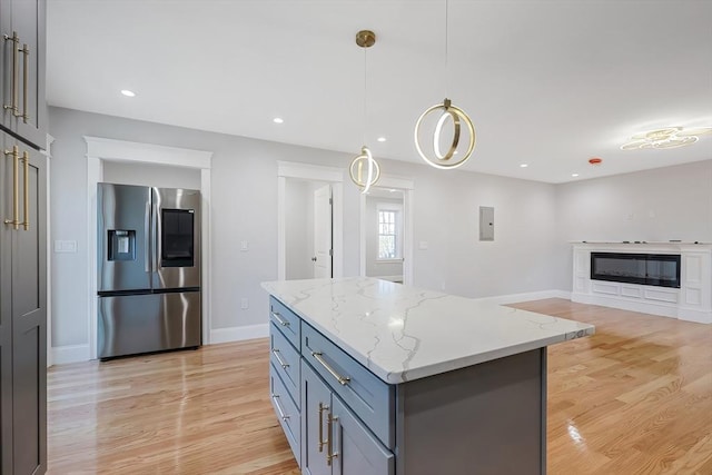 kitchen featuring light stone counters, light hardwood / wood-style flooring, pendant lighting, and stainless steel refrigerator with ice dispenser