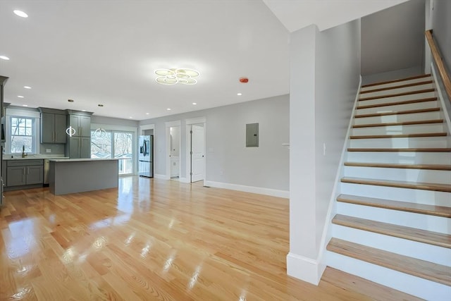 unfurnished living room with a healthy amount of sunlight, sink, electric panel, and light hardwood / wood-style flooring