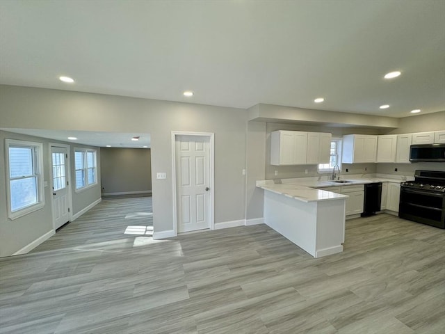 kitchen featuring sink, white cabinetry, light stone counters, black appliances, and kitchen peninsula