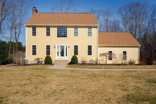 view of front of property featuring entry steps, a chimney, a front yard, and a shingled roof