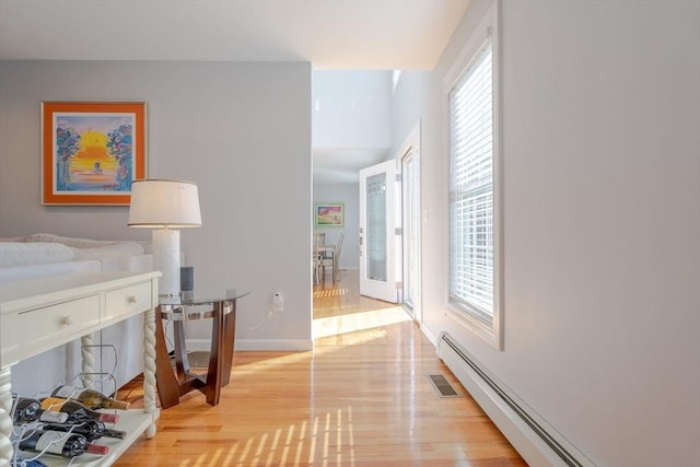 hall with a wealth of natural light, a baseboard radiator, baseboards, and light wood finished floors