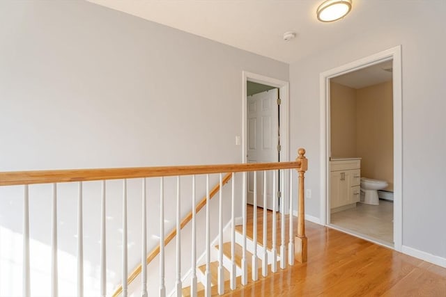 corridor featuring an upstairs landing, light wood-type flooring, and baseboards